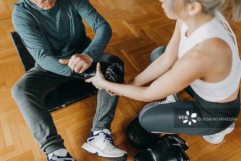 在年轻女性私人教练的协助下，年长男人进行锻炼图片素材