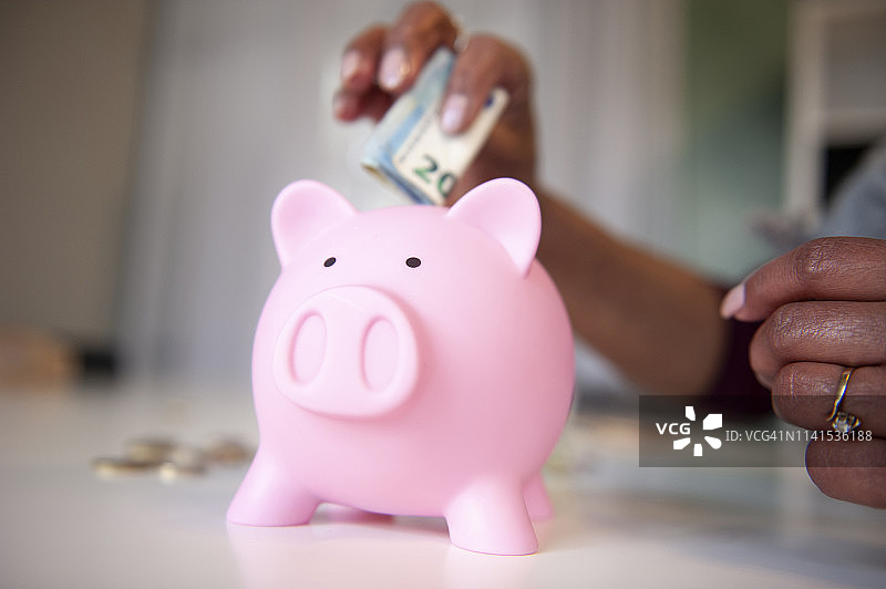 中年妇女把钱放进她的存钱罐里图片素材