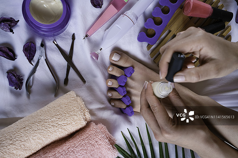 为有白色脚趾甲的女性进行足部护理，带有脚趾分离器图片素材