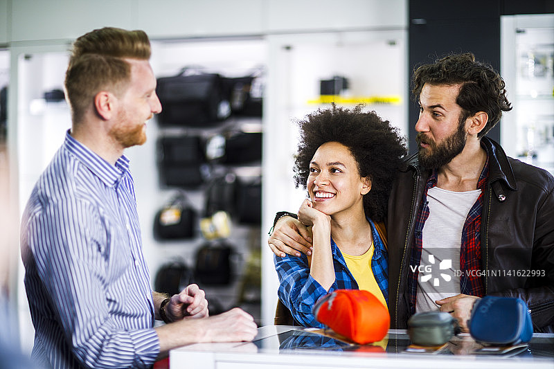年轻夫妇在商店店员的帮助下挑选相机包图片素材