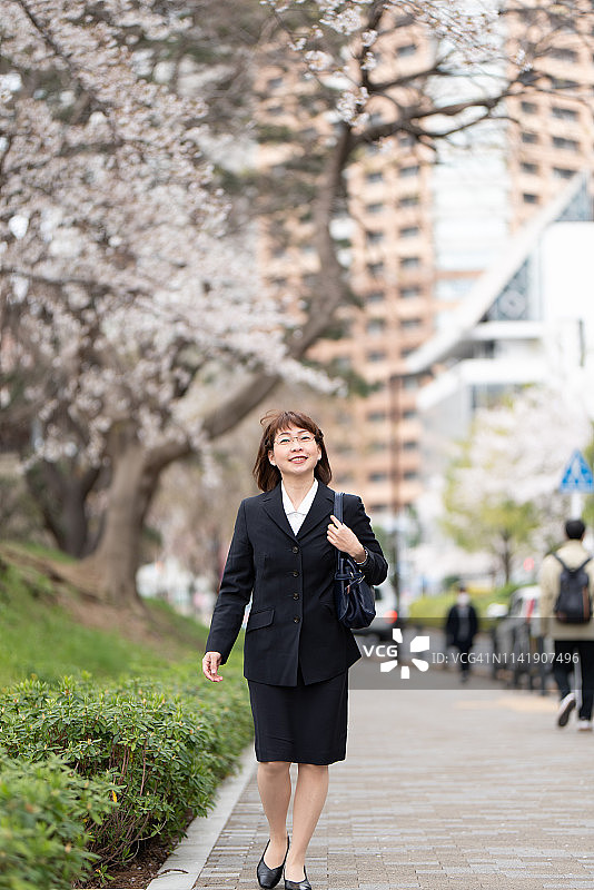女商人在樱花盛开的街道上行走图片素材
