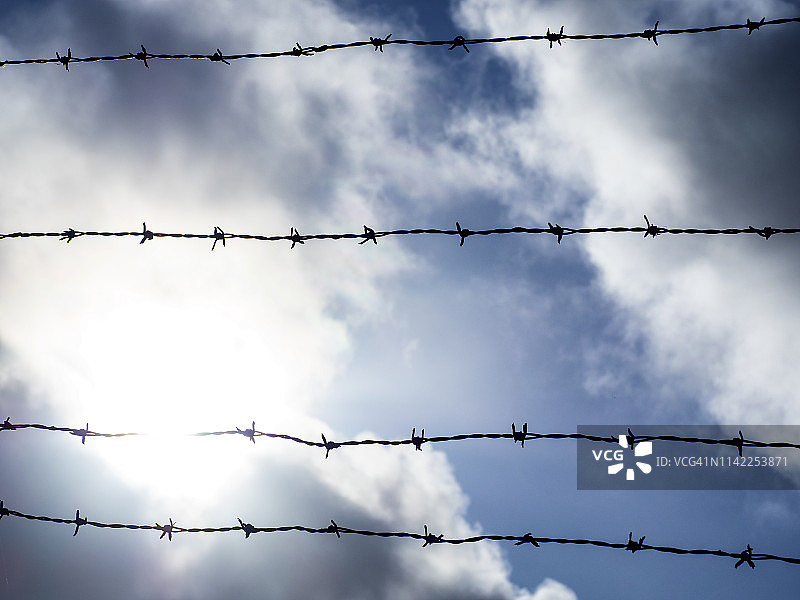 多云戏剧性天空下的带刺铁丝网低角度视图图片素材