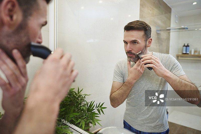在浴室里用电动剃须刀刮胡子的中年男人，波兰德比察图片素材