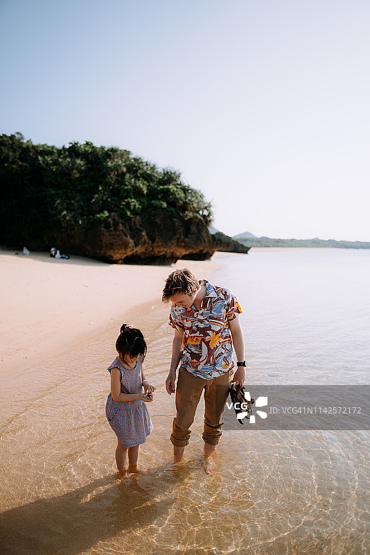 学龄前女孩与叔叔在冲绳热带海滩上捡拾海滩垃圾图片素材