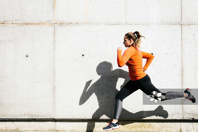 在水泥墙前跑步的年轻女运动员图片素材