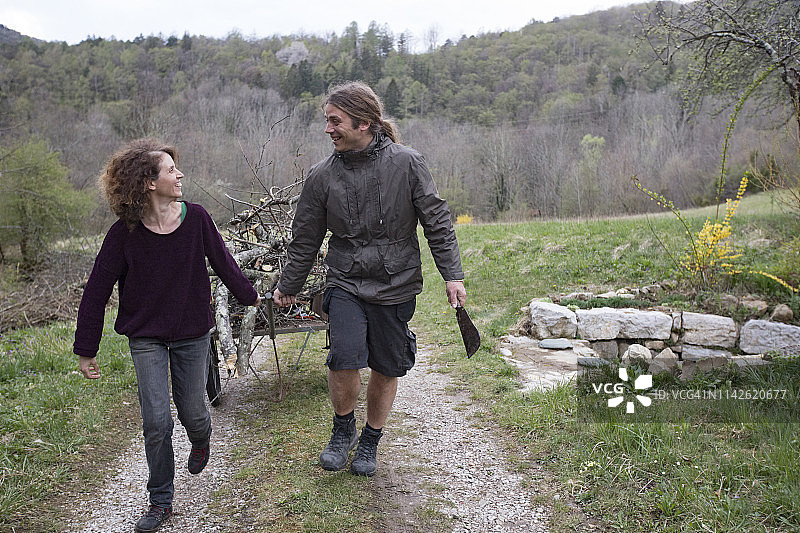 微笑的中年夫妇在乡村道路上拉着装满木柴的推车图片素材