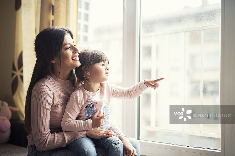 母女一起在家看着窗外，快乐地微笑图片素材