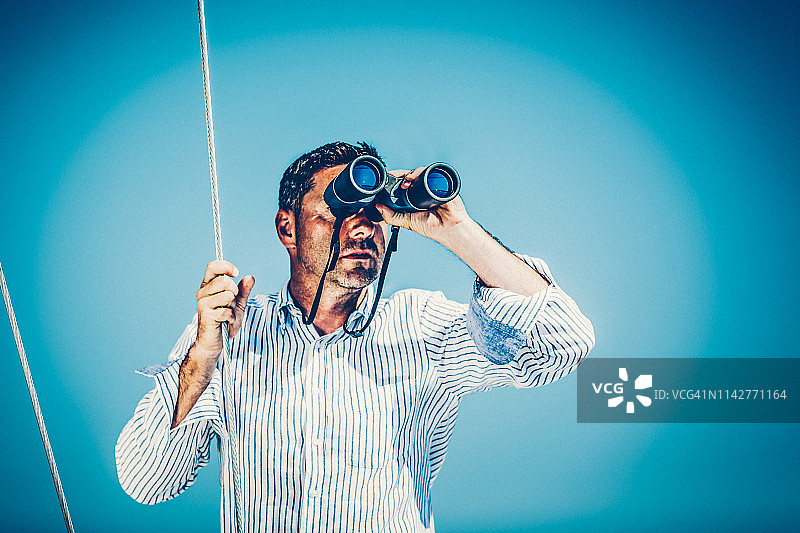 在帆船上使用双筒望远镜的帅气男人图片素材