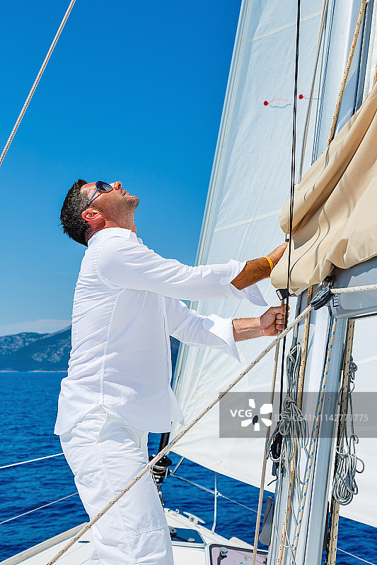 英俊的男人在帆船上扬起主帆图片素材