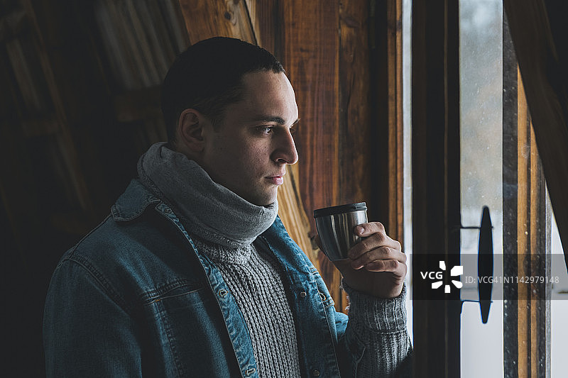 年轻男人穿冬装在小屋看窗外图片素材