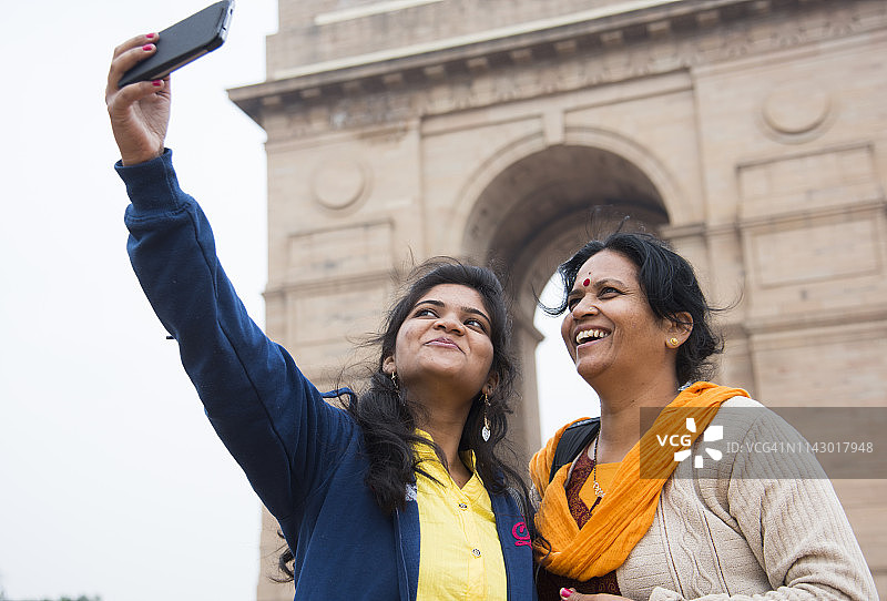 两名印度妇女在新德里印度门前用智能手机自拍图片素材