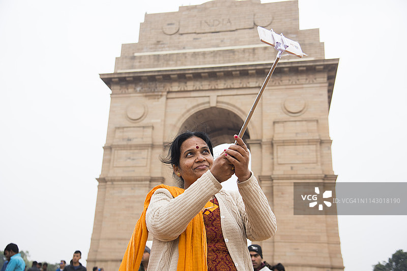 女人在新德里印度门前用自拍杆和智能手机自拍图片素材