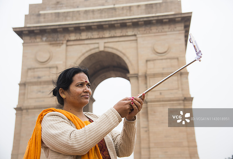 女人在新德里印度门前用自拍杆和智能手机自拍图片素材
