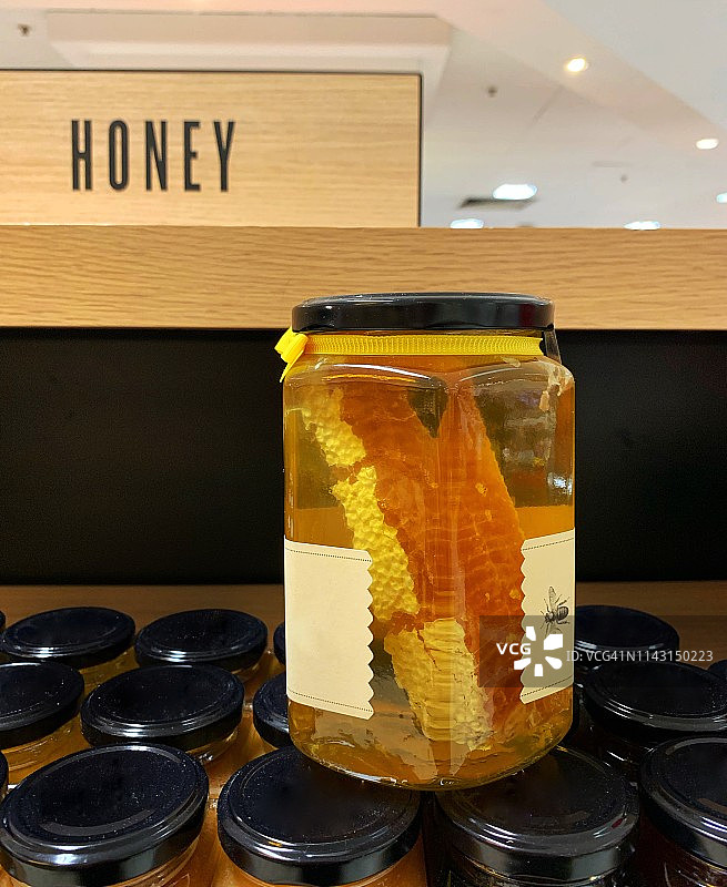 堆放在蜂蜜标志前的蜂蜜罐：金色有机蜂蜜与蜂窝图片素材