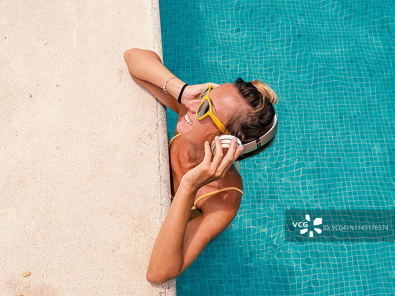 快乐的年轻女人在游泳池放松身心，用无线耳机听音乐图片素材