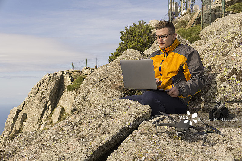 在岩石山上，仰视角度拍摄的男人用笔记本电脑控制四轴飞行器图片素材