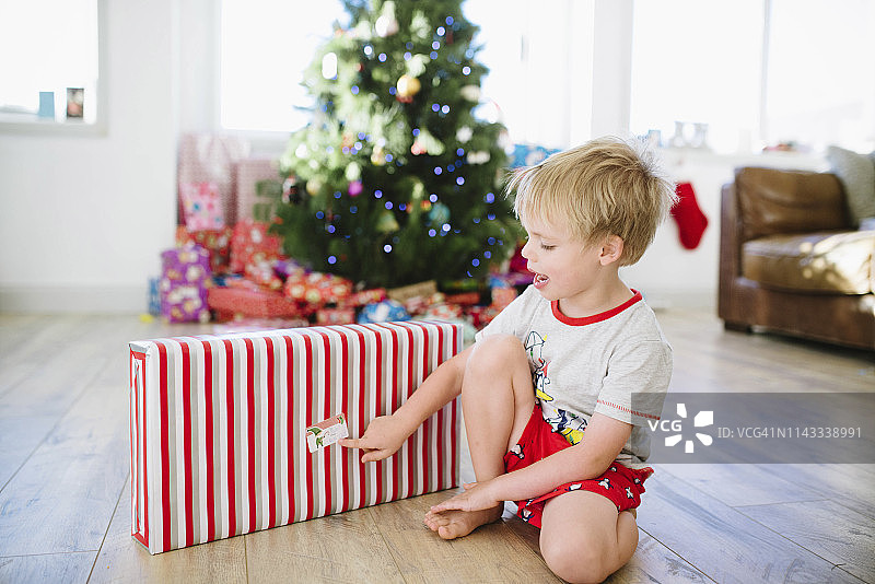 在家中硬木地板上拿着圣诞礼物的可爱男孩图片素材