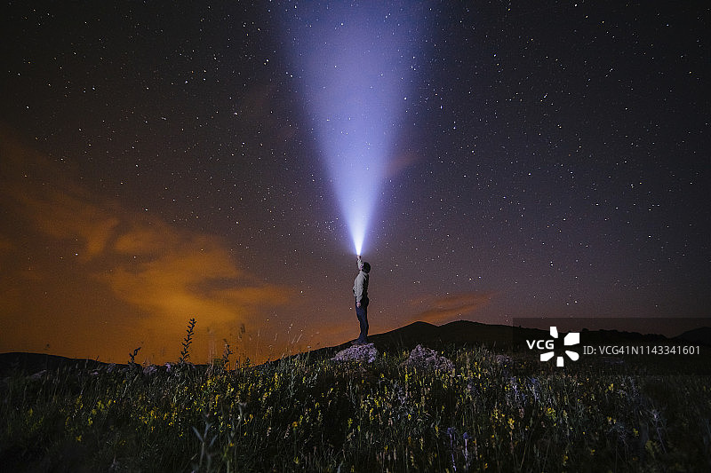 夜晚，男子站在山丘上用手电筒照亮星空侧视图图片素材