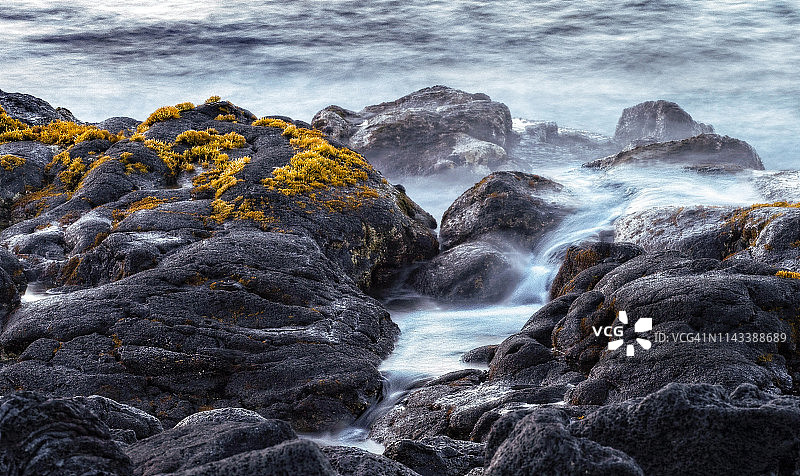 海浪无情地侵蚀和抚平这片岩石海岸线，海苔在熔岩上生长图片素材