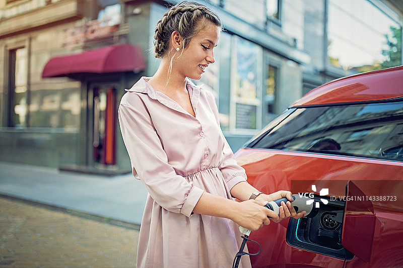 年轻女孩在城市里为她的电动汽车充电图片素材