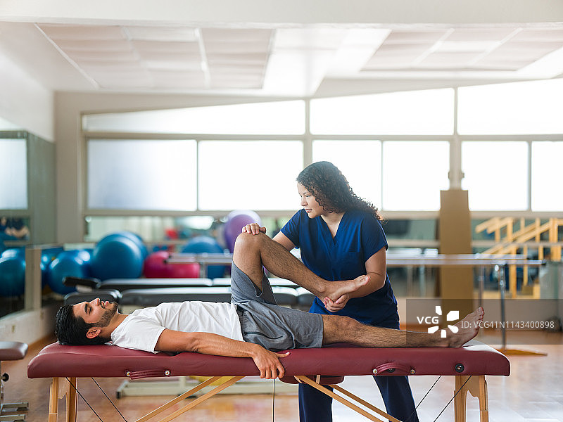 理疗师在按摩床上为患者伸展腿部图片素材