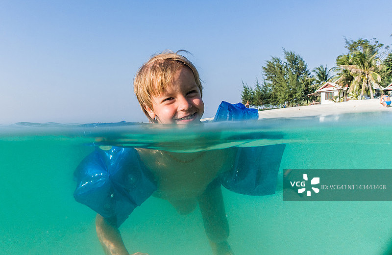 快乐的孩子在海里戴着臂带游泳图片素材