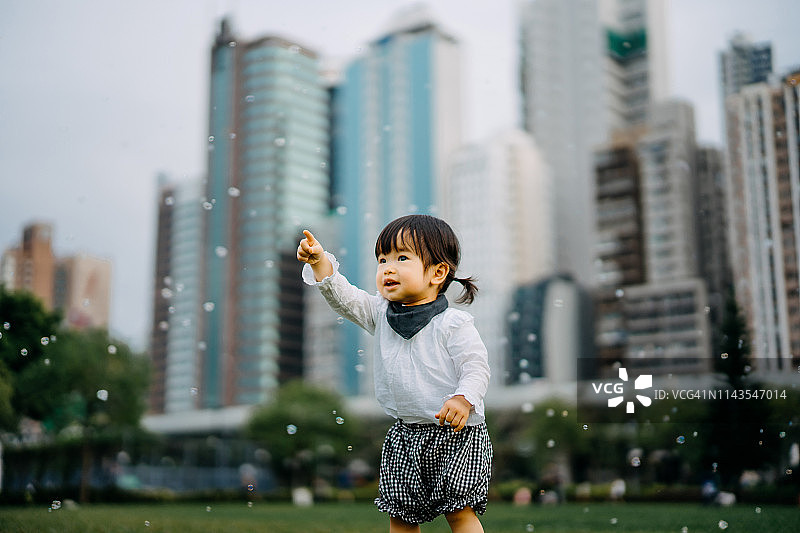 可爱女童在城市公园草坪上玩肥皂泡图片素材