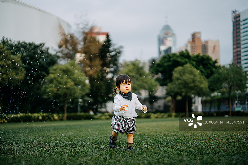 可爱女童在城市公园草坪上玩肥皂泡图片素材
