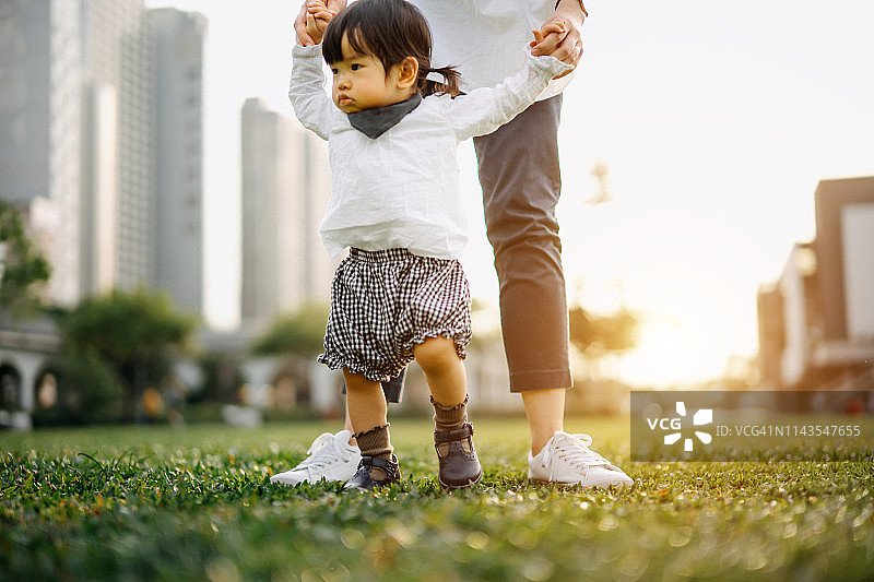 日落时分，母亲牵着女儿在城市公园漫步的肖像图片素材
