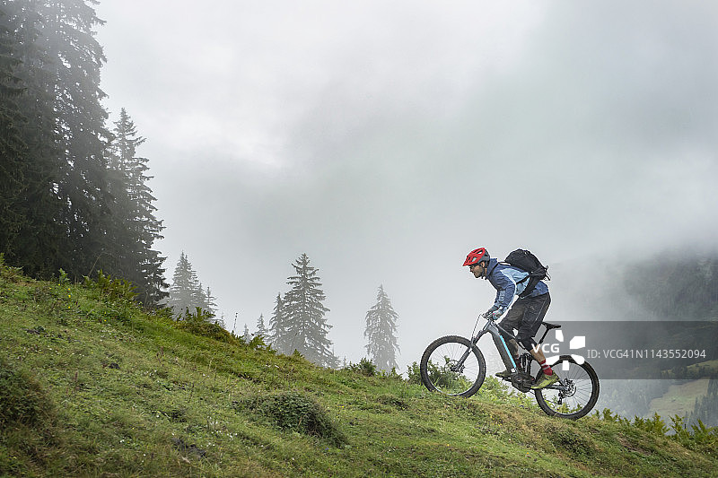 骑着电动自行车在山区上坡的男子，萨尔费尔登，蒂罗尔州，奥地利图片素材