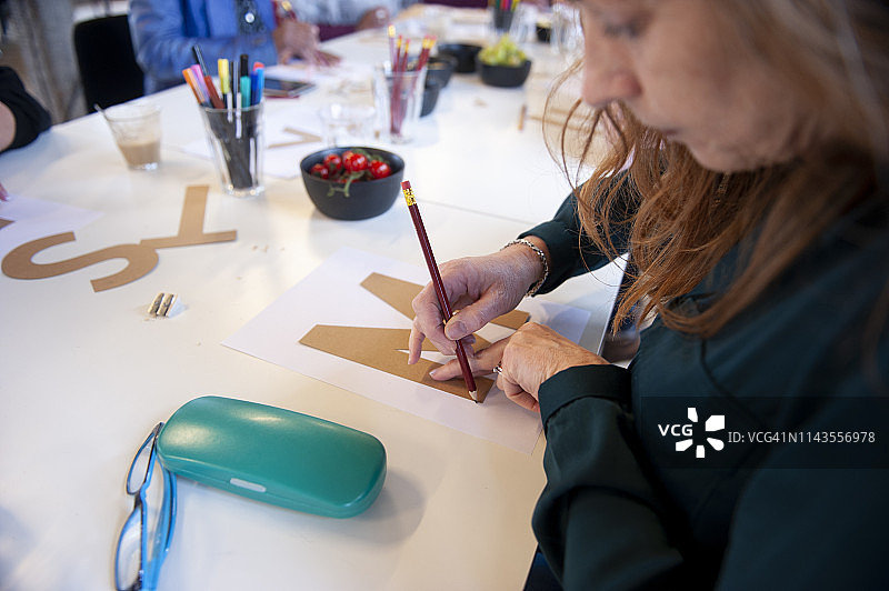 在一个手写字母的作坊里，中年妇女描摹纸板剪出的字母图片素材