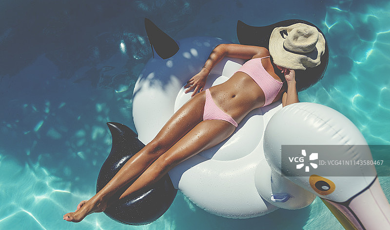 身穿粉色比基尼的女人在游泳池的白色充气垫上漂浮图片素材
