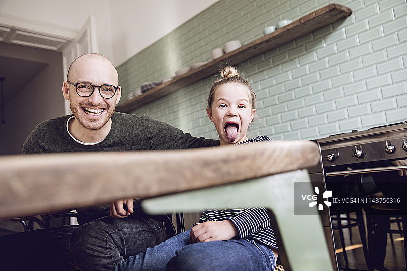 父女坐在厨房里，女儿做着鬼脸图片素材