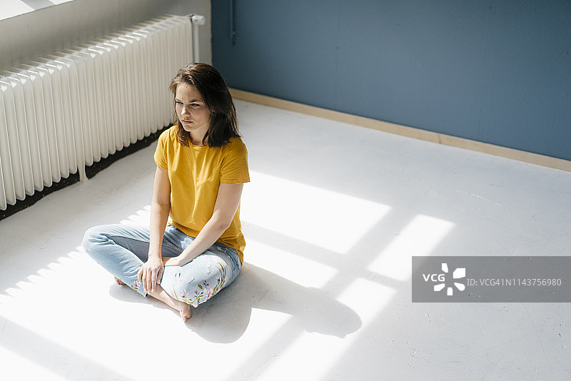 阳光下盘腿坐在地板上沉思的女人图片素材