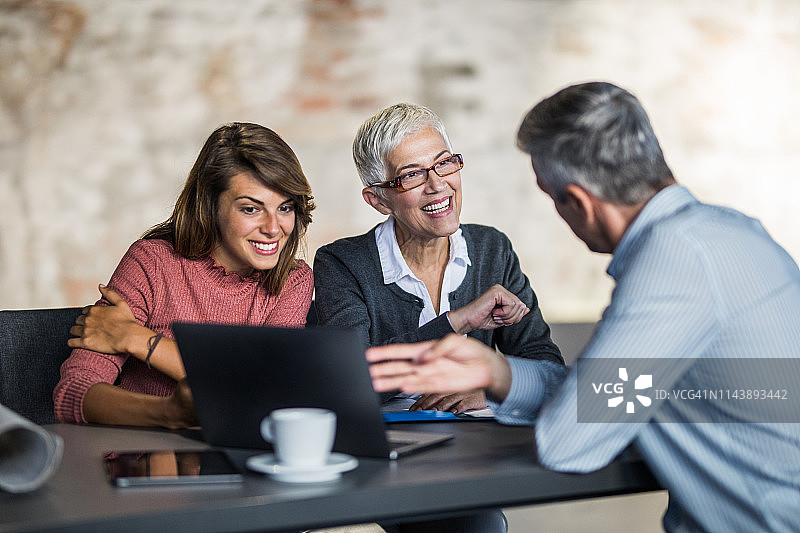 快乐的老年母亲和女儿与房地产经纪人一起使用笔记本电脑图片素材