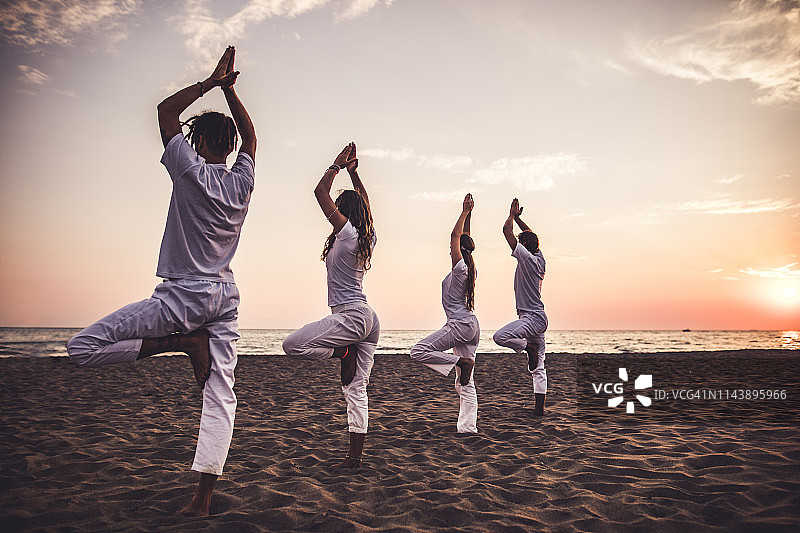日落时分，海滩上摆出树式姿势的运动人群的背影图片素材