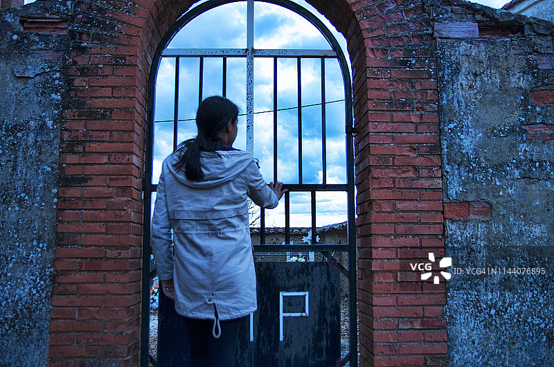 年轻女子透过墓地之门向里看图片素材
