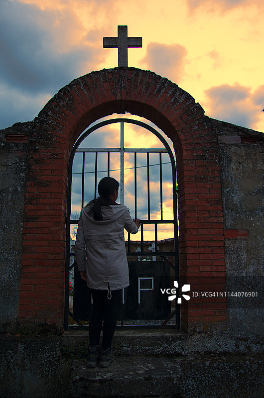 年轻女子透过墓地之门向里看图片素材