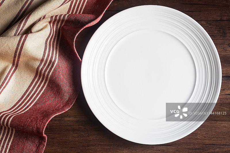 旧木棕色背景上的餐巾和空白白色餐盘，顶部视图图片素材