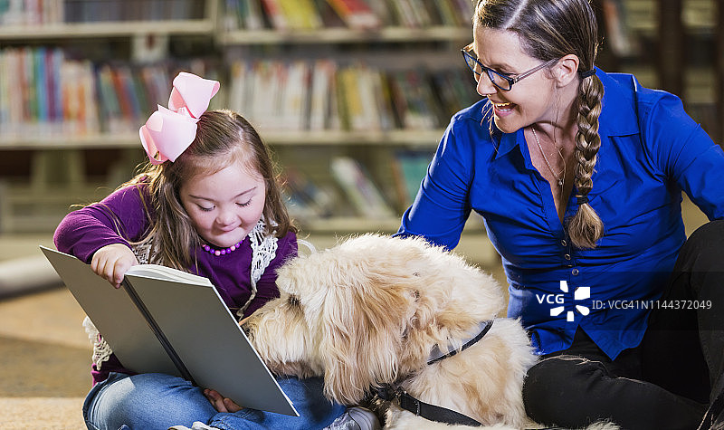在图书馆和治疗犬在一起的唐氏综合征女孩图片素材