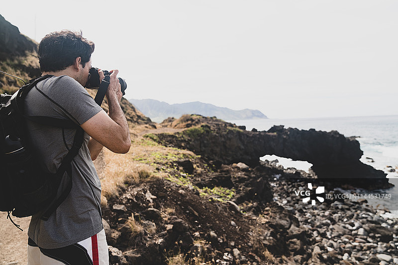 年轻人在岩石海滩上用单反相机拍照图片素材