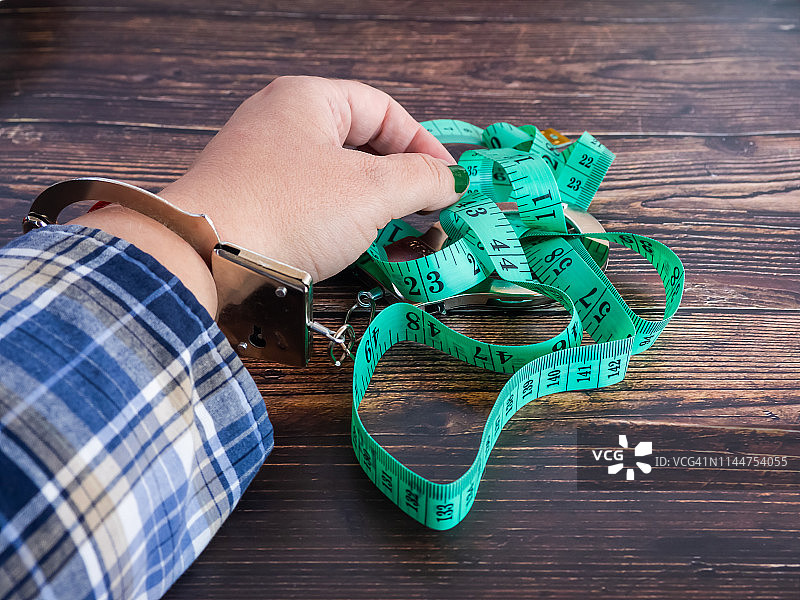 戴着手铐，拿着卷尺的人。减肥概念图片素材