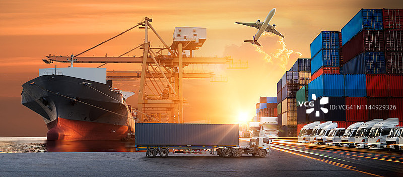 集装箱卡车在港口进行商业物流和运输，日出时船坞内有集装箱货轮和货机以及起重机桥，物流进出口和运输行业背景图片素材