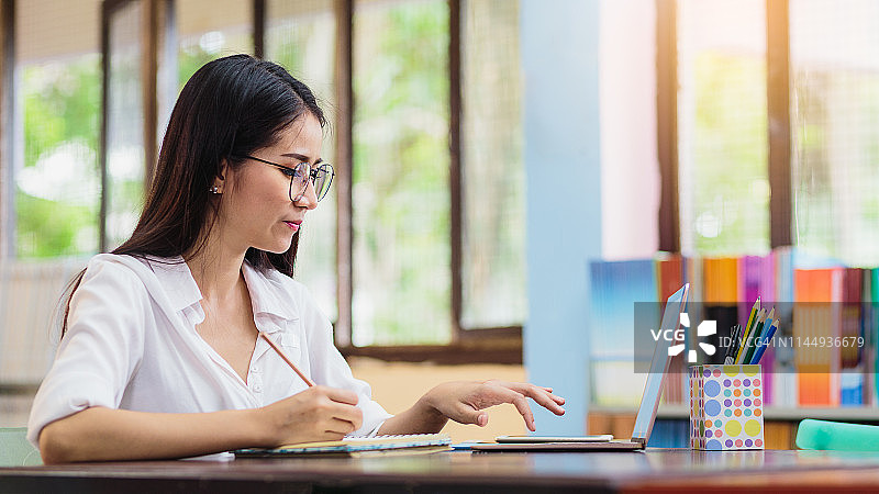 年轻亚洲女人图书馆学习研究写笔记图片素材