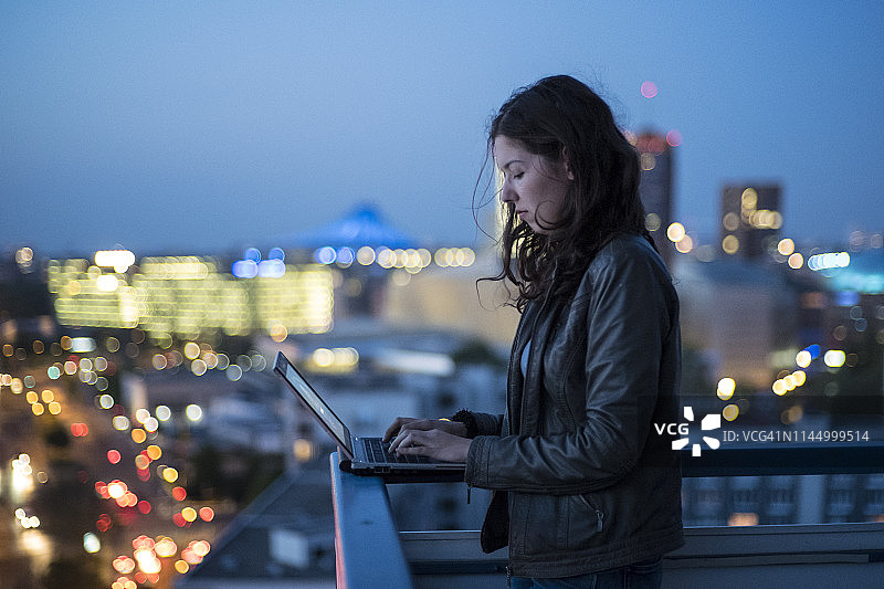 年轻女人在笔记本电脑上打字，背景是柏林城市夜景图片素材