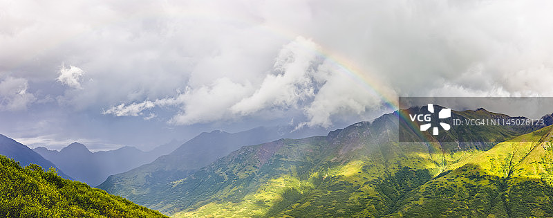一道彩虹穿过大气光,背景是郁郁葱葱的绿色山坡,位于阿拉斯加中南部的哈atcher山口图片素材