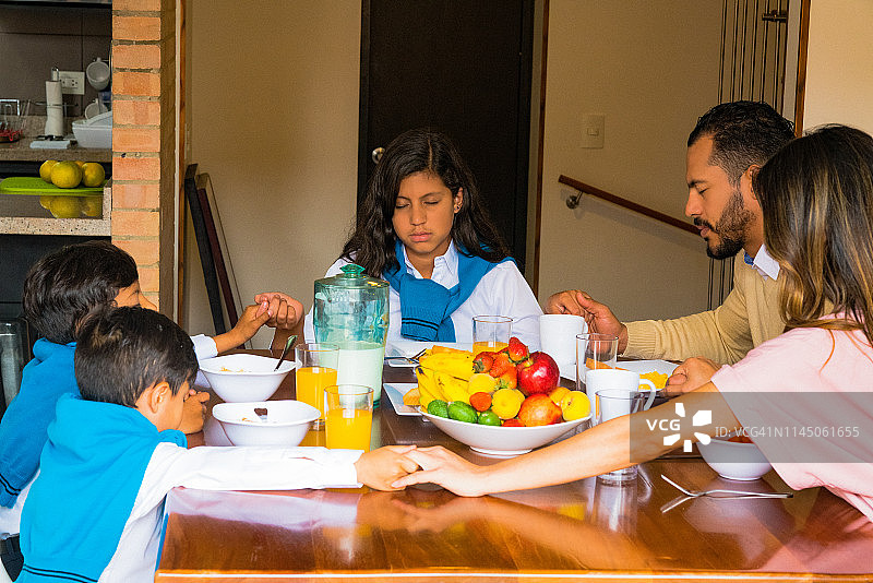 拉丁家庭在摆满食物的桌子旁闭着眼睛祈祷图片素材