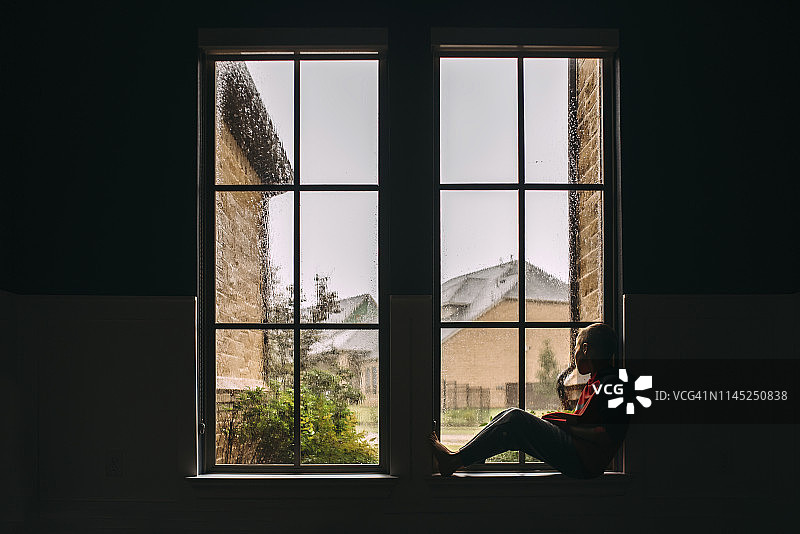 男孩雨天在家中靠窗向外看的侧面照图片素材
