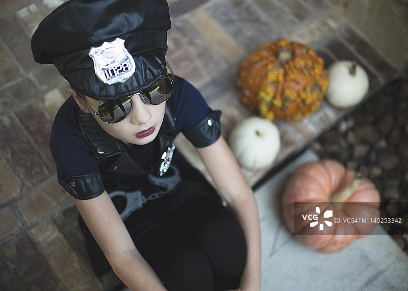 万圣节期间，在院子里南瓜旁，穿着警察服装和太阳镜的女孩（高角度拍摄）图片素材