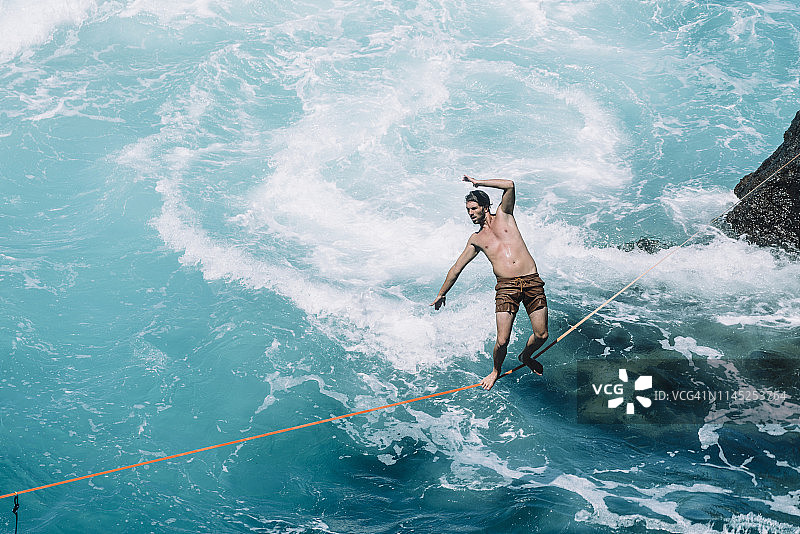 在晴朗的一天，快乐的年轻男人在海上绳索上行走图片素材